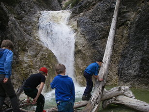 Kinder balancieren auf alten Baumstämmen vor einem Wasserfall 