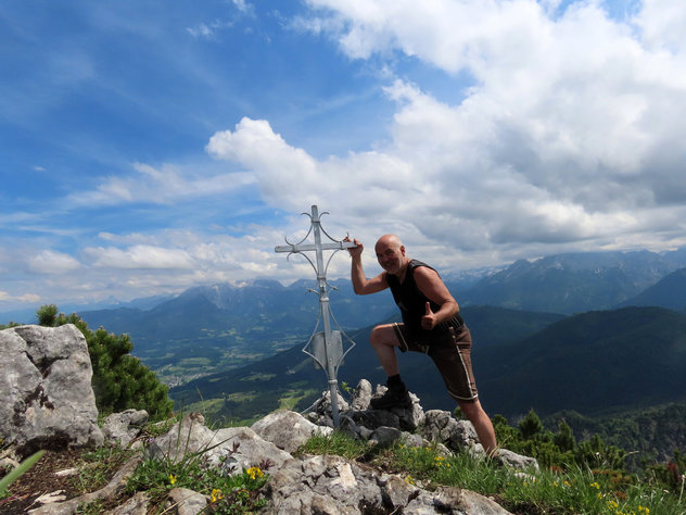 Bergsteiger an einem kleinen, eisernen Gipfelkreuz