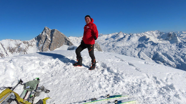 Skibergsteiger auf einem hohen winterlichen Gipfel mit imposanter Bergkulisse im Hintergrund 