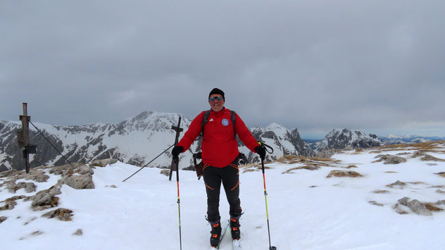 Skibergsteiger mit roter Jacke auf flachen Berggipfel an einem wolkigen Tag 