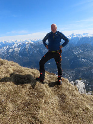 Braungebrannter Bergsteiger auf einem Berggipfel, im Hintergund schneebedeckte Berge 