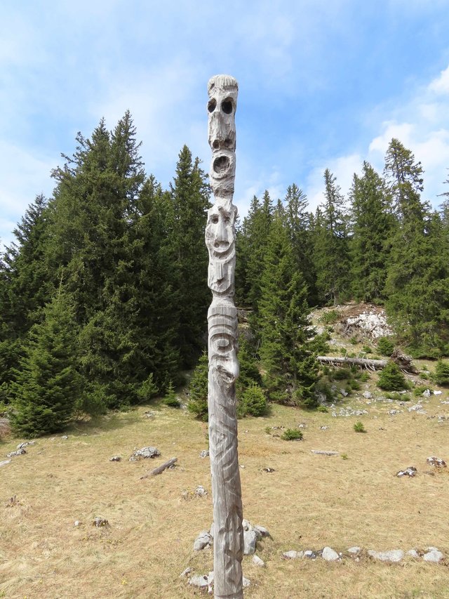 Beschnitzter Holzpfahl mit vielen Gesichtern auf einer Bergwaldlichtung