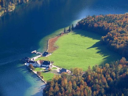 Grüne Halbinsel im Bergsee mit Häusern und kleiner Kirche