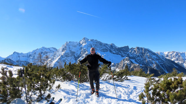 Skibergsteiger steht strahlend im Sonnenschein, hinter ihm ein imposantes, winterliches Bergmassiv