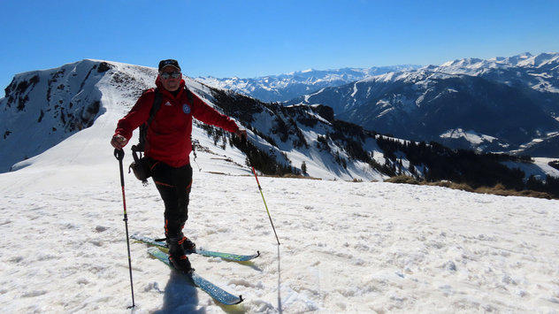 Skitourengeher mit roter Jacke vor imposanter, winterlicher Berglandschaft im Sonnenschein 