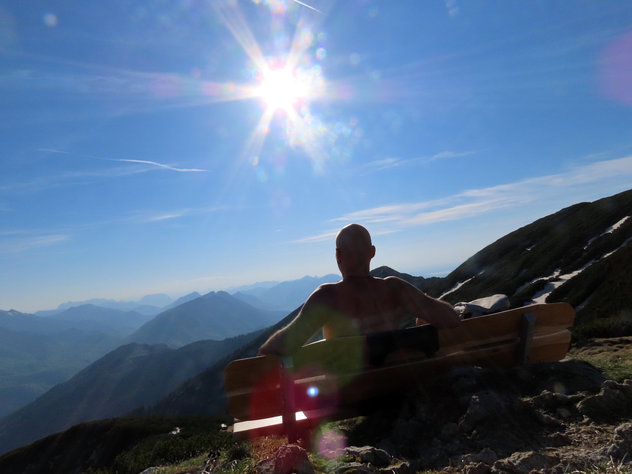 Bergwanderer sitzt auf Bank in der Sonne und schaut in die Bergwelt 