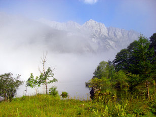 Nebel auf einem Bergsee, darüber schemenhaft Felsberge