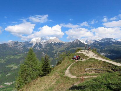 Stark frequentierter Berggipfel, dahinter schneebedeckte Berggipfel