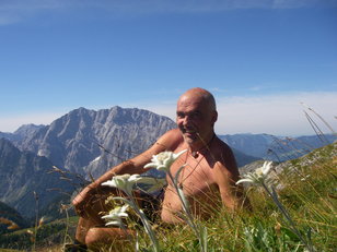 Halbnackter Bergwanderer liegt in Bergblumenwiese mit Edelweiß, im Hintergrund ein markanter Berg 