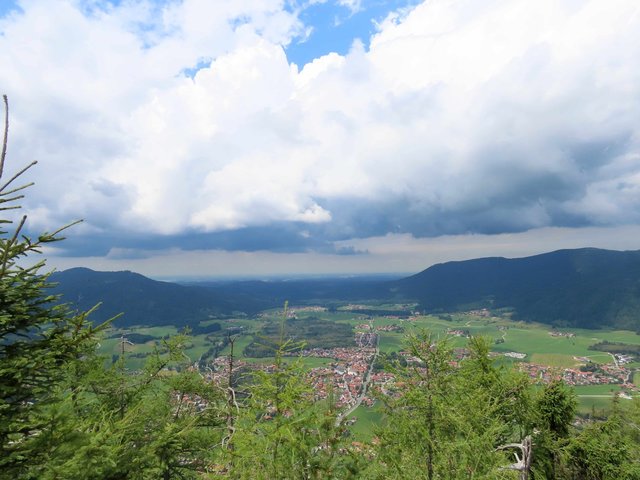 Ausblick von Berggipfel auf Ortschaft mit Wolken im Hintergrund 