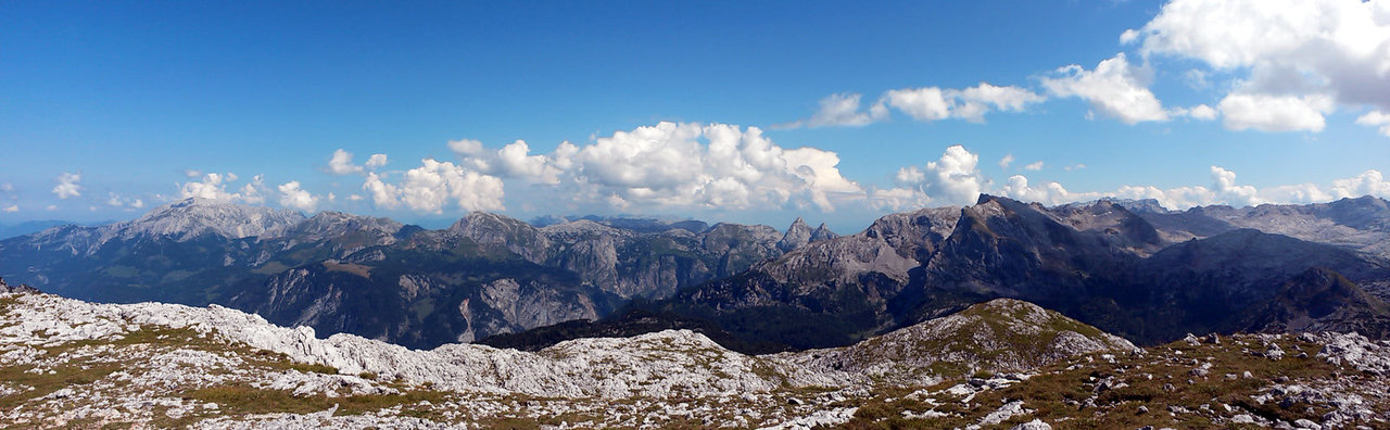 Weite Berglandschaft mit vielen Gipfeln und Wolken darüber