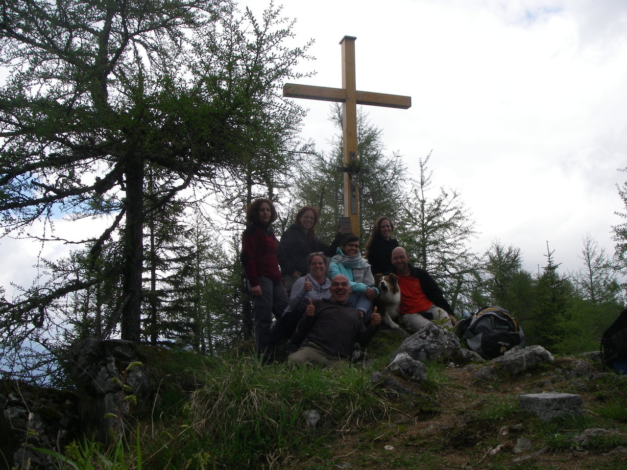 Bergwandergruppe an einem Gipfelkreuz eines bewaldeten Gipfels